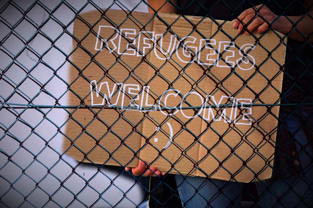 Pappschild hinter einen Drahtzaun mit der Aufschrift "Refugees Welcome"